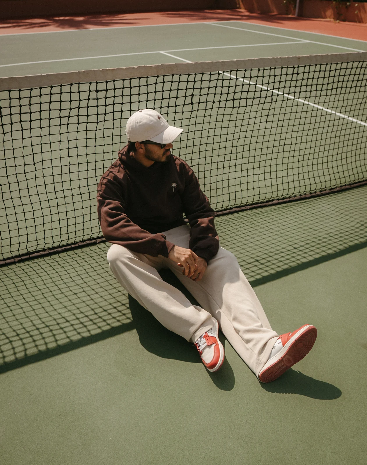 Model seated on a tennis court in a dark hoodie